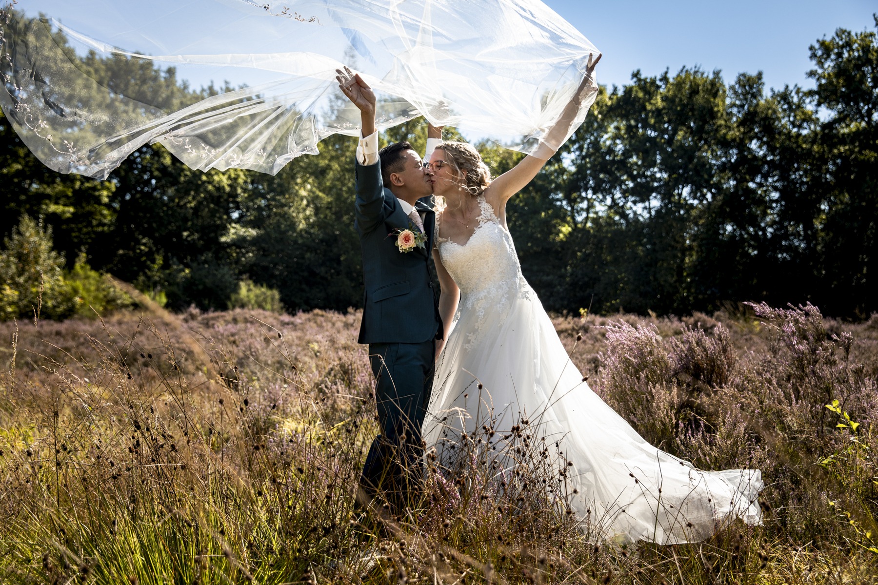 Kleurrijke bruidsreportage met foto van bruidspaar op de heide. De sluier van de bruid door de wind in de lucht.