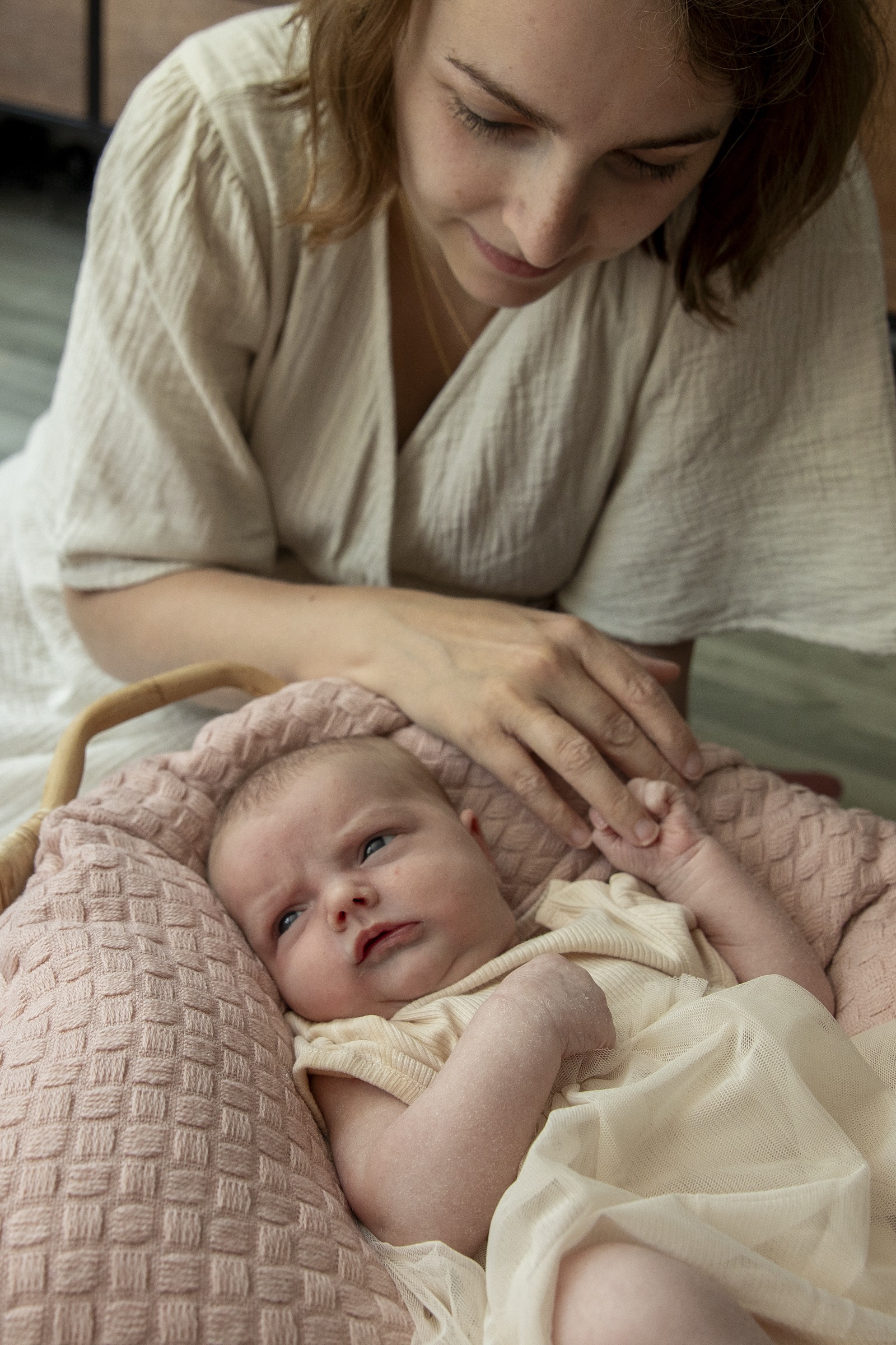 Moeder kijkt naar haar baby die op een rose kleedje ligt en ze houdt haar handje vast.