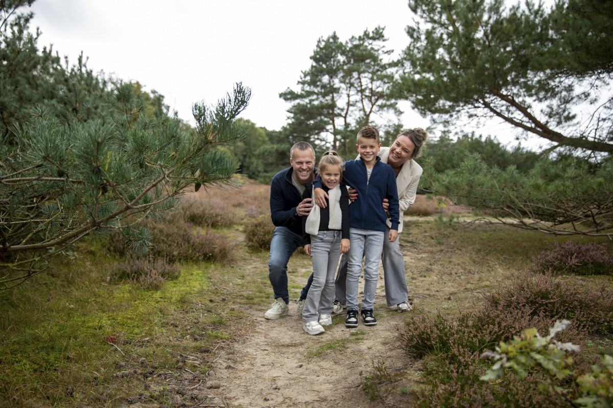 Gezin op de foto op een zandpad met op de achtergrond heide en bomen.